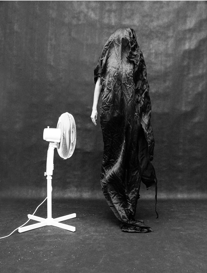 Figure covered in black fabric with white fan