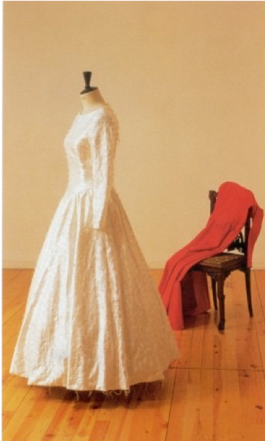 White dress on a mannequin next to chair with red fabric draped on it.