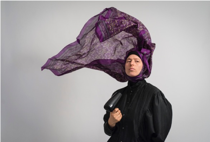 Woman blowdrying her purple headscarf.
