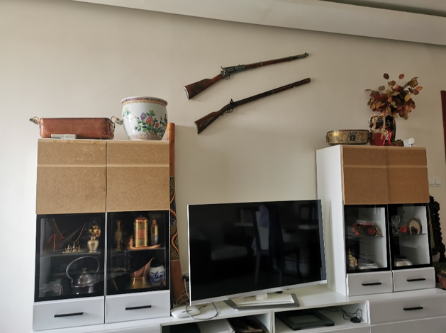 Decorative shelves with containers and a TV screen, with two rifles hanging above on the wall