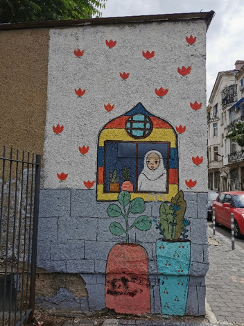Mural wall showing a woman looking out a window with two potted plants