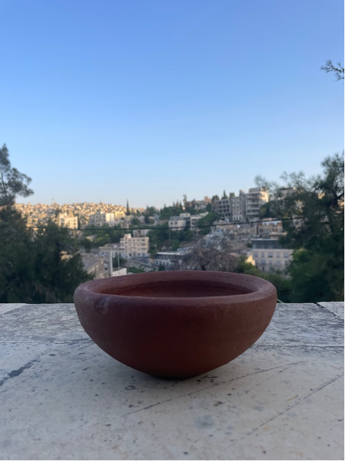 A clay pot sits on a ledge with buildings in the background.