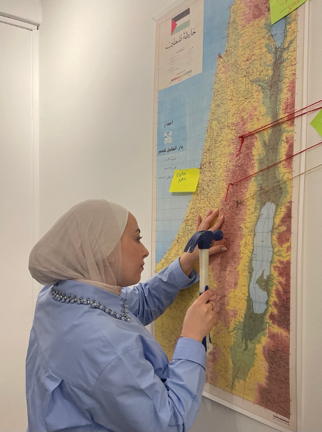 A woman uses a hammer to nail a pin into a map.