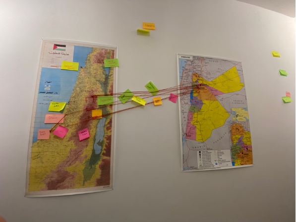 Two maps are situated next to each other on a wall. Red strings and sticky notes indicate connections between two locations.
